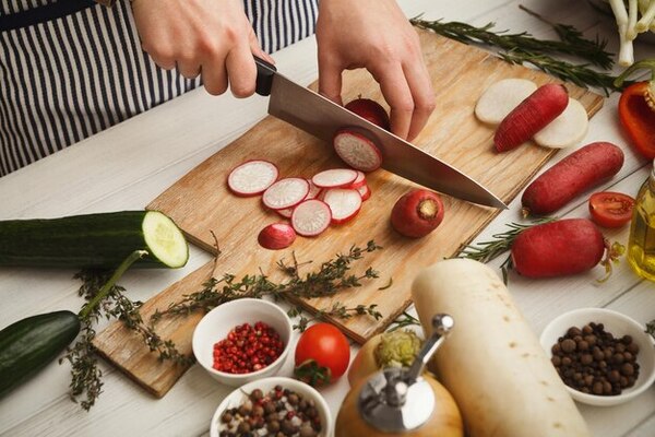 Persona adulta cortando verduras frescas en una cocina luminosa con tabla de madera